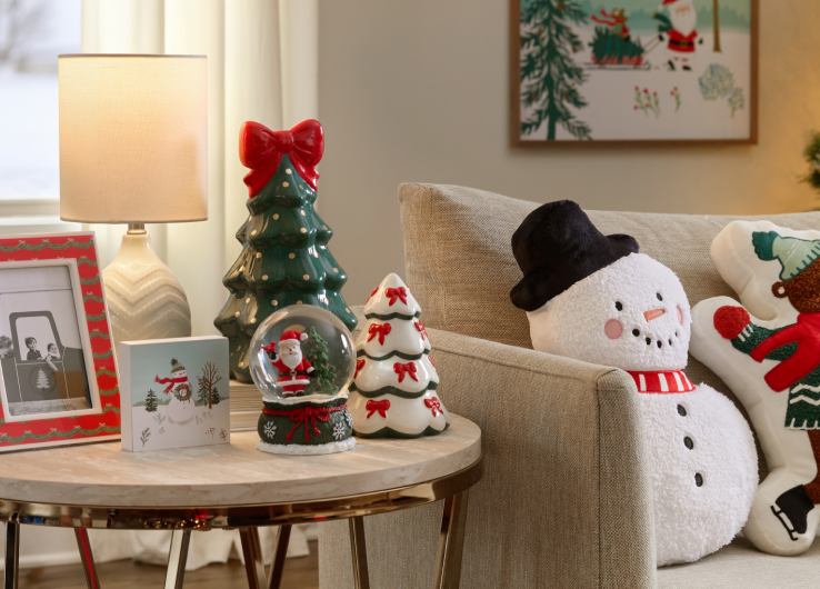Christmas home décor featuring snowman and gingerbread pillows, tabletop trees and snow globe