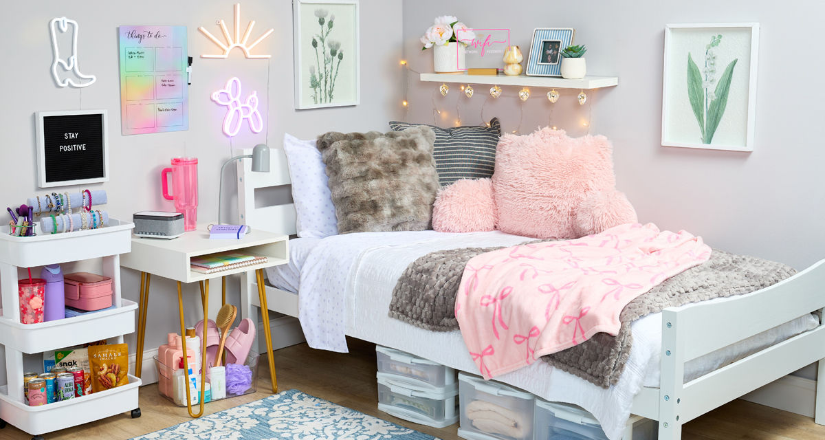Dorm room decorated with pastel and neautral tones: pink & gray throws, pink furry study pillow, white storage cart, wall lights, sheets & more.