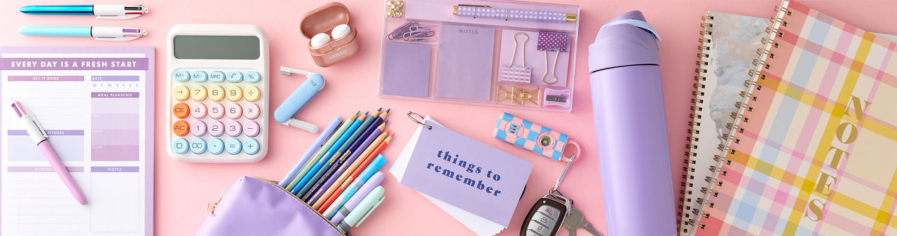 Pastel back-to-school supplies: spiral notebooks, purple pouch with colored pens & pencils, calculator, water bottle, earbuds & more.
