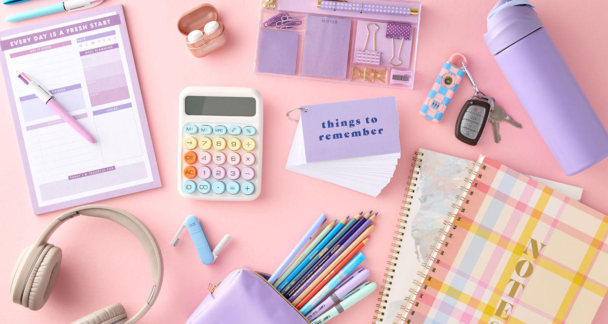 Pastel back-to-school supplies: spiral notebooks, purple pouch with colored pens & pencils, calculator, water bottle, earbuds & more.