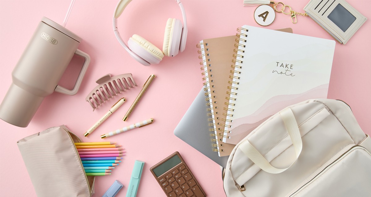 Neutral-toned back-to-school supplies: cream backpack, white headphones, spiral notebooks, tan pouch with colored pencils pastel highlighters, pens & more.