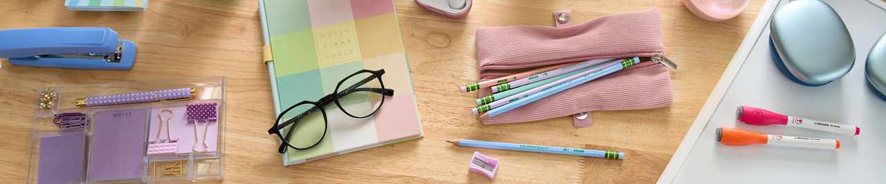 Pastel back-to-school supplies: spiral notebooks, purple pouch with colored pens & pencils, calculator, water bottle, earbuds & more.