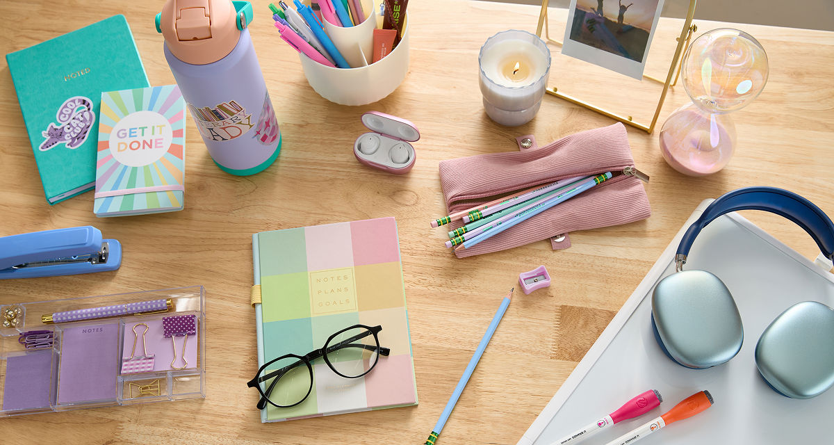 Pastel back-to-school supplies: spiral notebooks, purple pouch with colored pens & pencils, calculator, water bottle, earbuds & more.