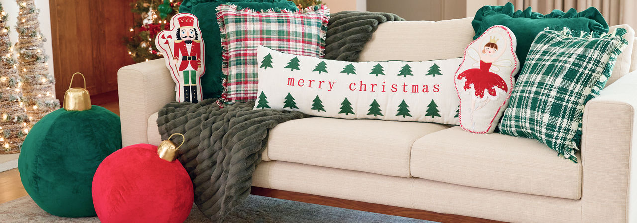 Christmas pillows in various shapes and designs on a sofa: red and greed jumbo ornament pillows, velvety green and plaid pillows, lumbar pillow, and more.