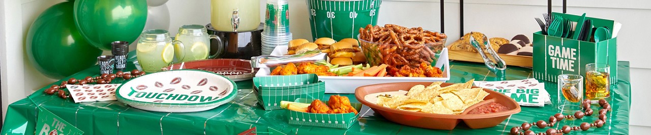 Big Game watch party table with footbal-themed balloons, ice bucket, party plates, cups, utensils, football platter & more from pOpshelf.