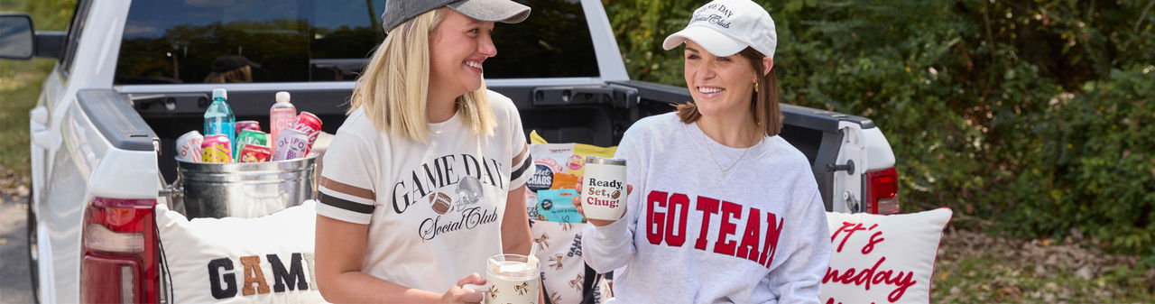 Girls at tailgating party with football-themed blankets, pillows, travel cups & apparel, and tailgating snacks.