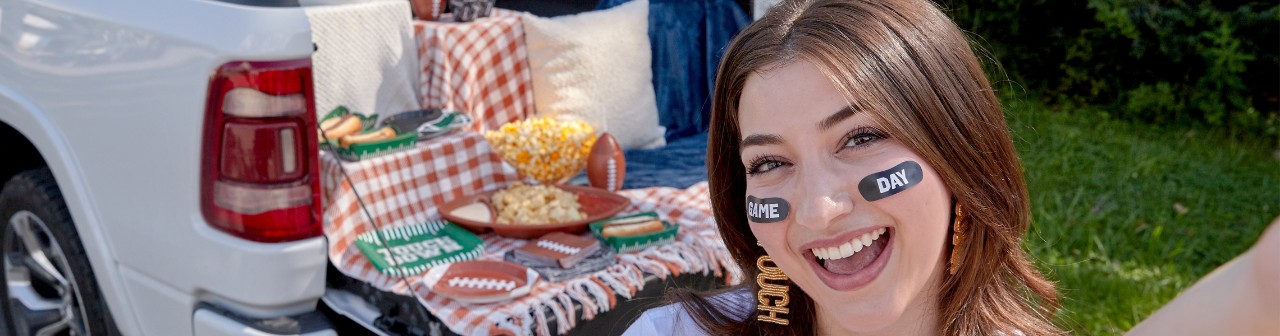 Girl at tailgating party with football-themed party supplies, clear  cross body bag with game sticker patches, and football-themed jewelry and face stickers.