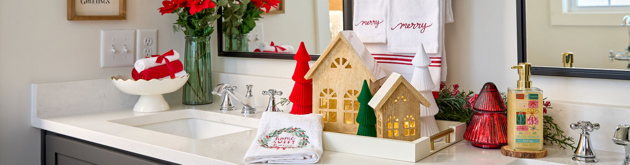 Bathroom decorated for Christmas with 3-piece "merry" towel set, candles, Christmas hand soap, wooden village houses, and more.