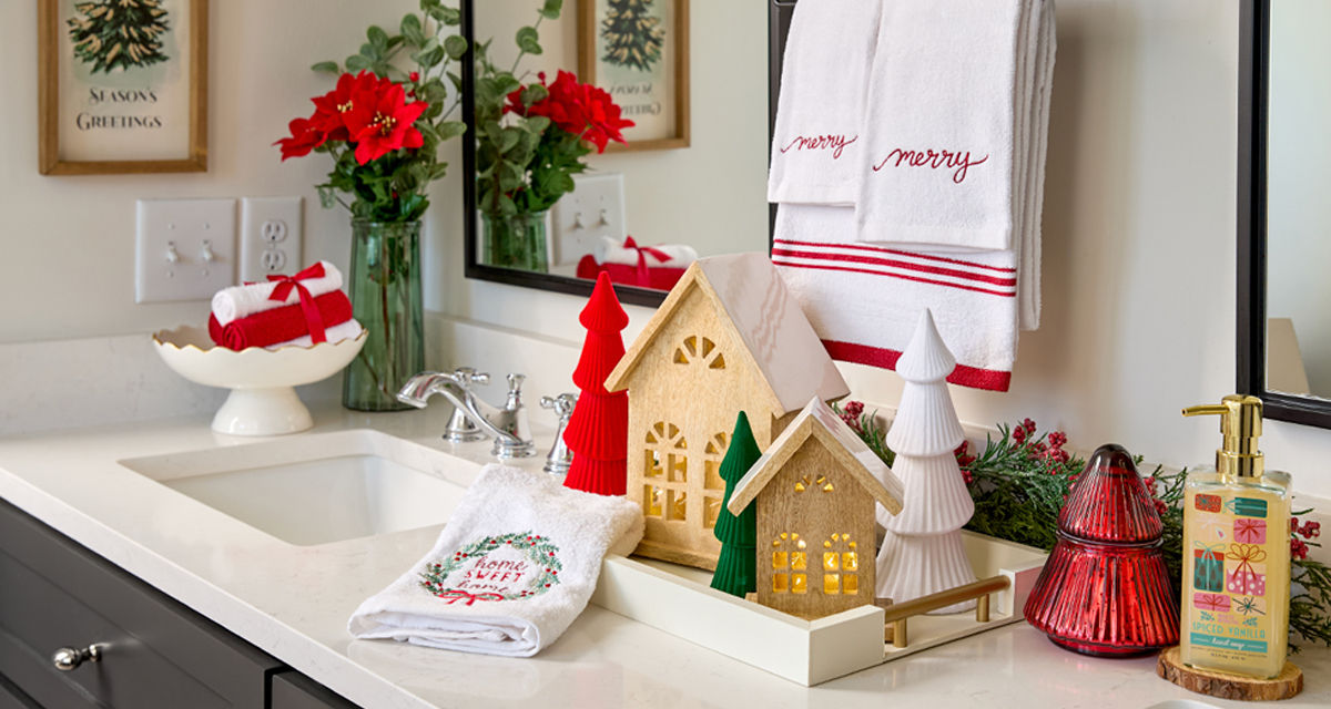 Bathroom decorated for Christmas with 3-piece "merry" towel set, candles, Christmas hand soap, wooden village houses, and more.