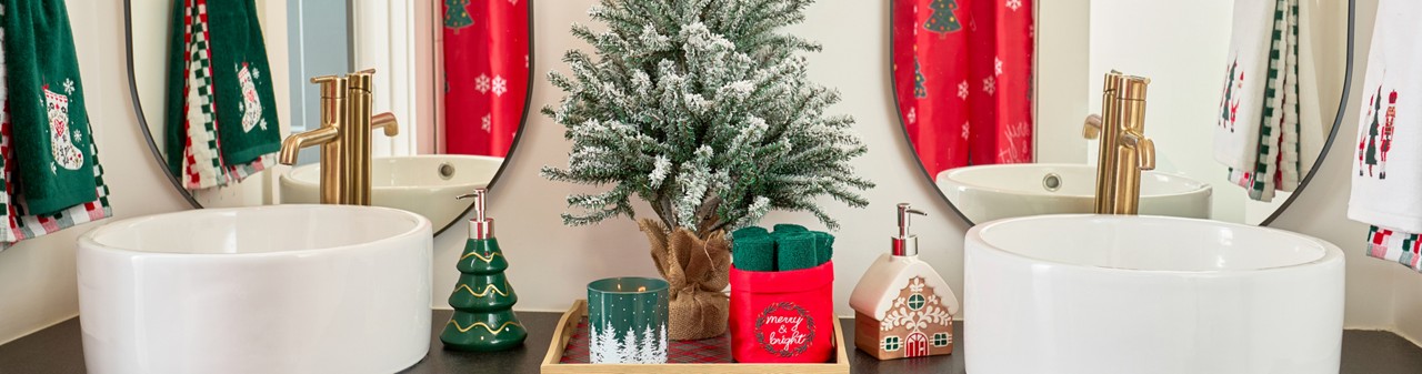 Bathroom decorated for Christmas with ferstive shower curtain, hand towels, bath rug, tree and gingerbread house soap pumps, and Christmas decor.