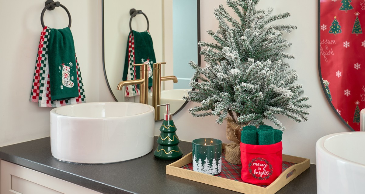 Bathroom decorated for Christmas with ferstive shower curtain, hand towels, bath rug, tree and gingerbread house soap pumps, and Christmas decor.