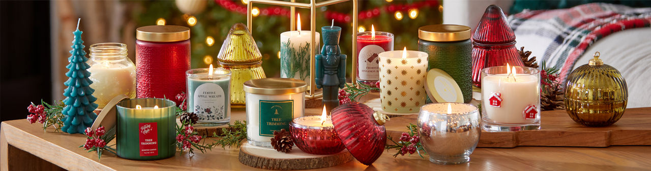 Christmas candles in various sizes, designs, and scents on a table in front of a Christmas tree.