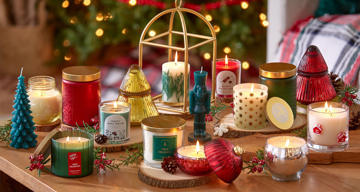 Christmas candles in various sizes, designs, and scents on a table in front of a Christmas tree.