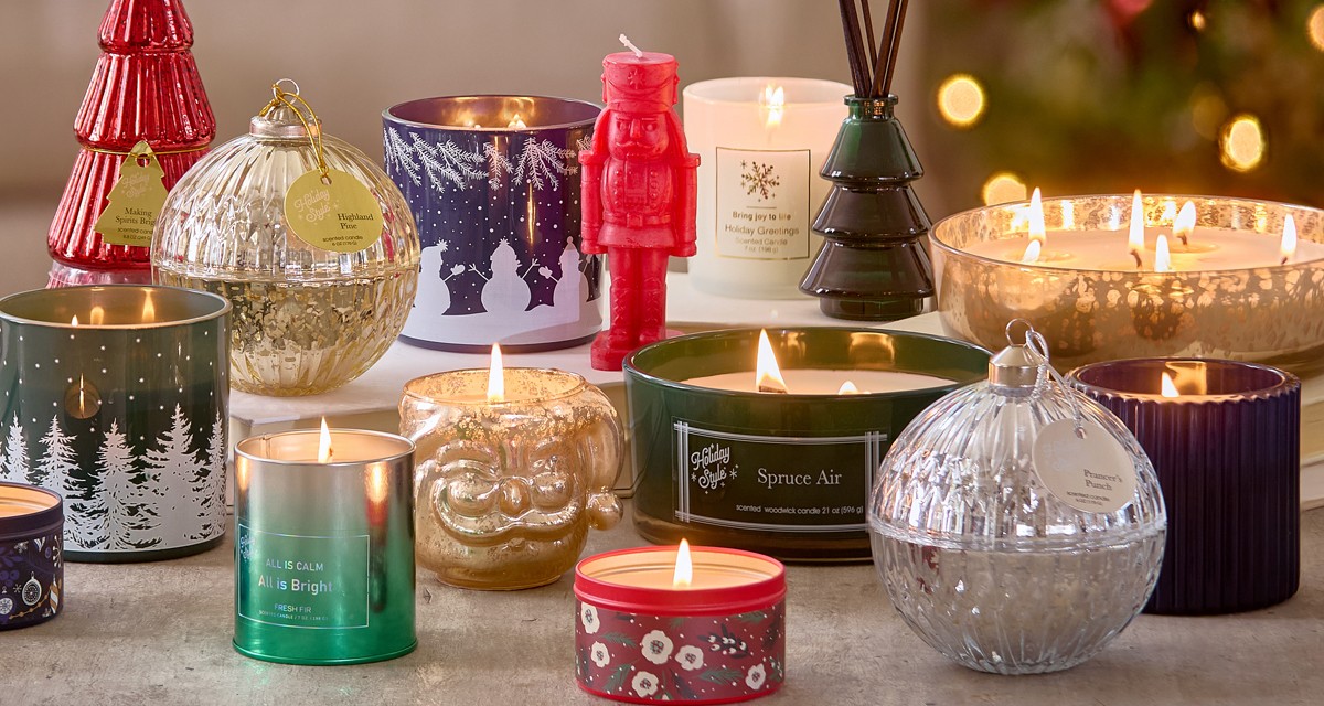 Christmas candles in various sizes, designs, and scents on a table in front of a Christmas tree.