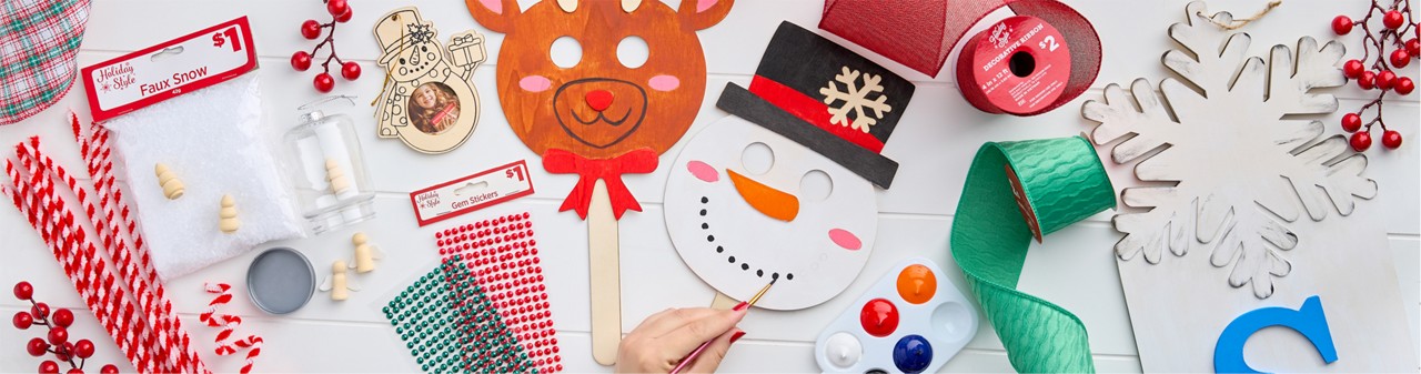 Christmas craft supplies: wooden handheld DIY masks, DIY snowflake porch leaner, green, red, and plaid wired ribbon, DIY plastic fillable ornaments & more.