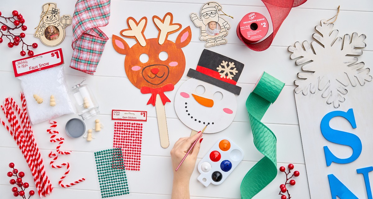 Christmas craft supplies: wooden handheld DIY masks, DIY snowflake porch leaner, green, red, and plaid wired ribbon, DIY plastic fillable ornaments & more.