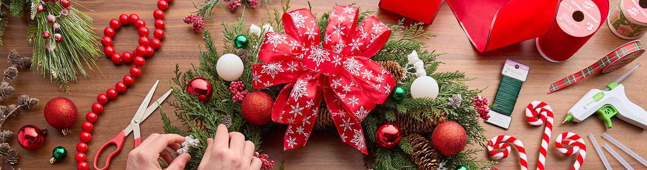 Christmas craft supplies: wooden handheld DIY masks, DIY snowflake porch leaner, green, red, and plaid wired ribbon, DIY plastic fillable ornaments & more.