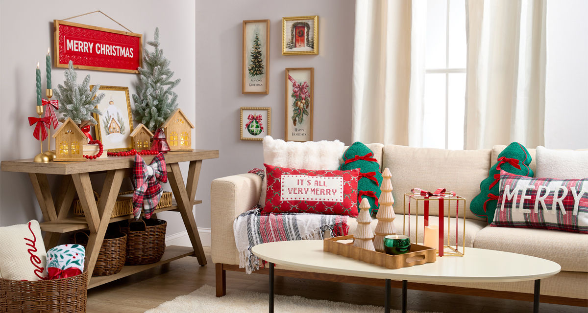 Room decorated for Christmas with wooden trees and village houses, festive pillows & throws, candles, metal lantern, and more. 