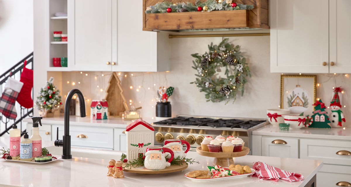 Christmas mixing bowl, wooden cake stand and lazy susan, tree-shaped charcuterie tray, village house cookie jar, Santa mugs, gingerbread man salt & pepper shakers, and more in a kitchen decorated for Christmas.