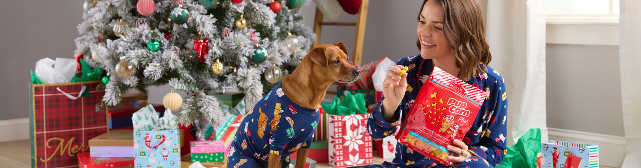 Girl and dog in front of Christmas Tree in matching PJs with pet toys and treats.