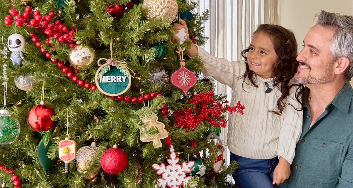 Dad and daughter decorating a Christmas tree with a variety of ornaments from pOpshelf.