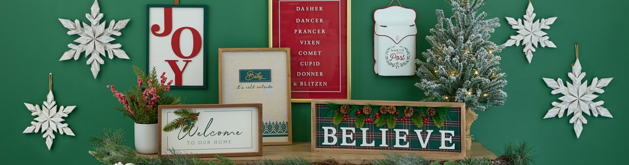 Christmas signs and wall decor in various sizes and designs on a green wall.