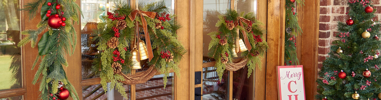 Front door with two faux pine wreaths with pinecones, red berries, and gold bells and faux pine garland with red berries and ornaments. 