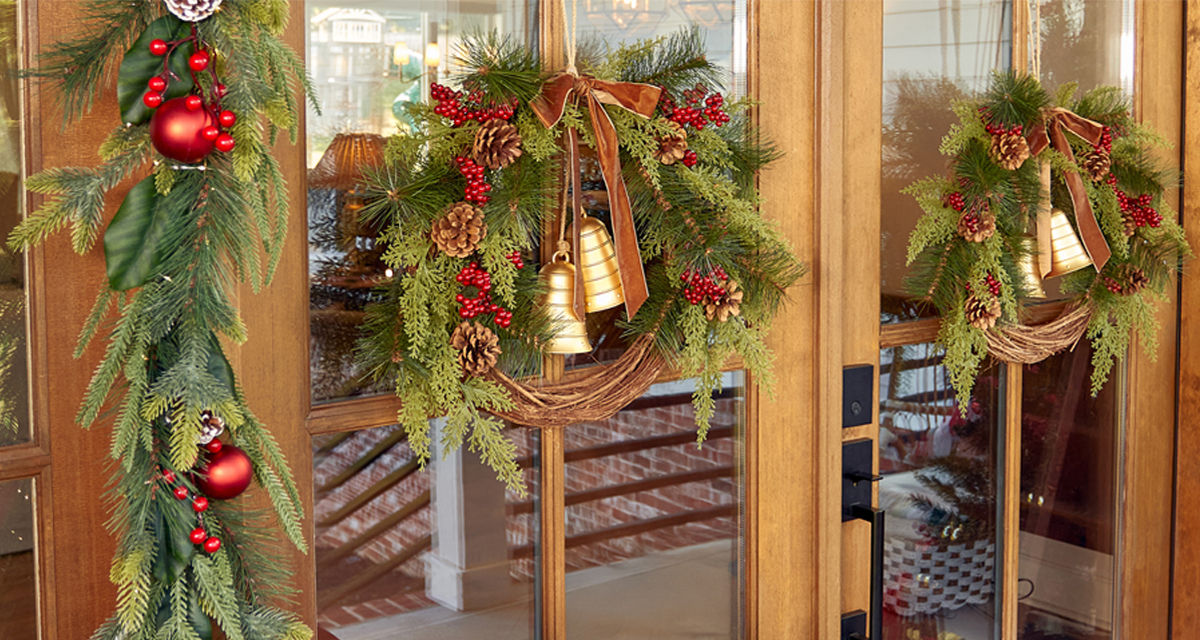 Front door with two faux pine wreaths with pinecones, red berries, and gold bells and faux pine garland with red berries and ornaments. 