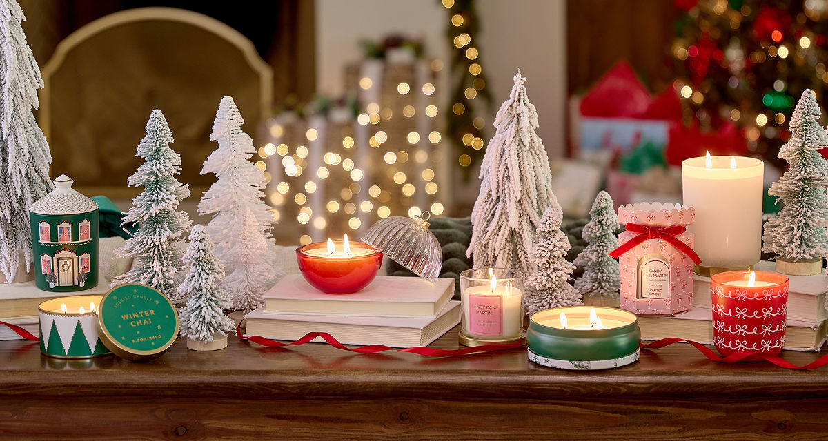 Christmas candles in various sizes, designs, and scents on a table in front of a Christmas tree.