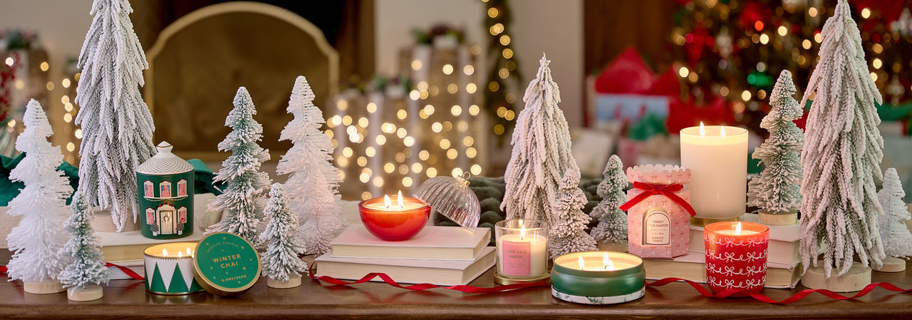 Christmas candles in various sizes, designs, and scents on a table in front of a Christmas tree.