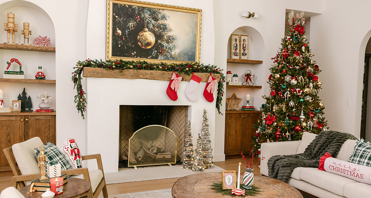 Living room decorated for Christmas with faux pine garland, stockings, tree full or ornaments, festive Christmas pillows and throws, candles, tabletop decor & more.
