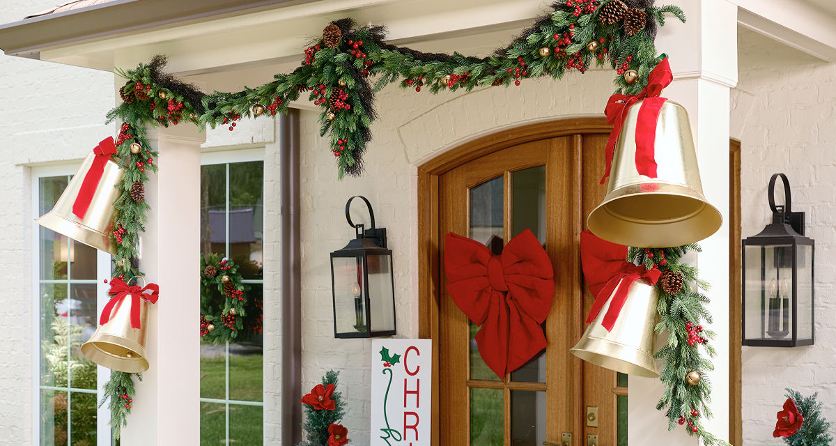 Front porch decorated for Christmas with wreaths garland, coir mats, rattan decor, pillows, bells & more.
