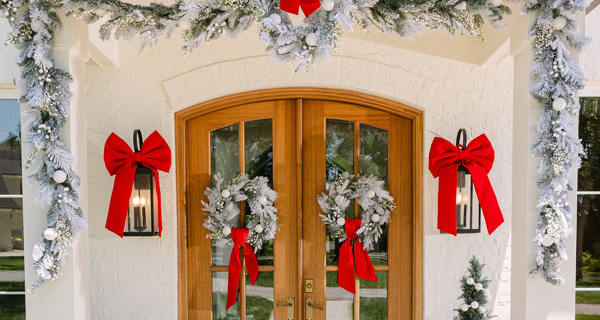Front door with two snowy faux pine wreaths with white ornaments and white berries, and faux snowy pine garland with white berries and ornaments. 