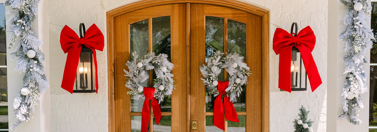 Front door with two snowy faux pine wreaths with white ornaments and white berries, and faux snowy pine garland with white berries and ornaments. 