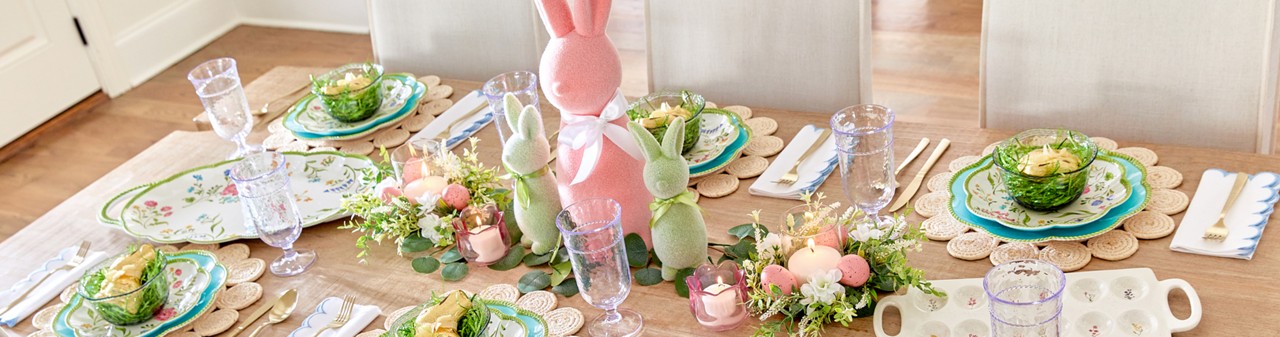 Easter brunch table set with scalloped floral plates, flocked Easter bunny centerpiece, Easter tulip candles, and Eater floral arrangements.