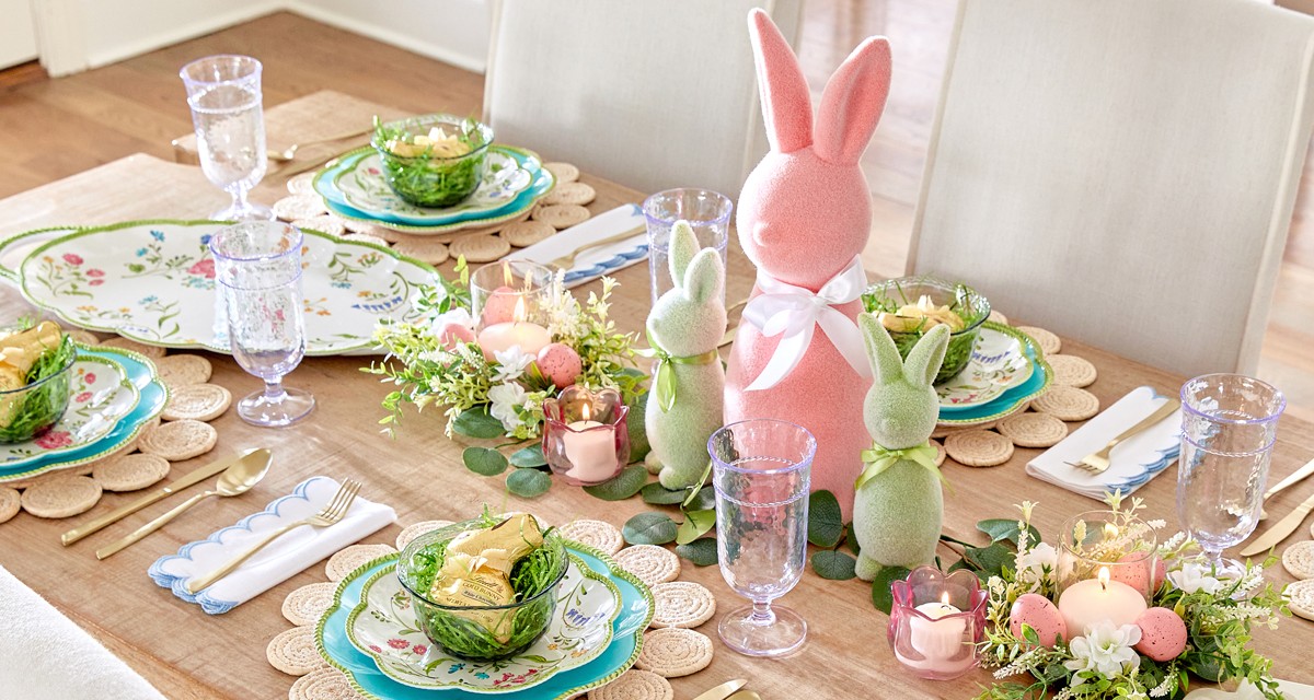 Easter brunch table set with scalloped floral plates, flocked Easter bunny centerpiece, Easter tulip candles, and Eater floral arrangements.
