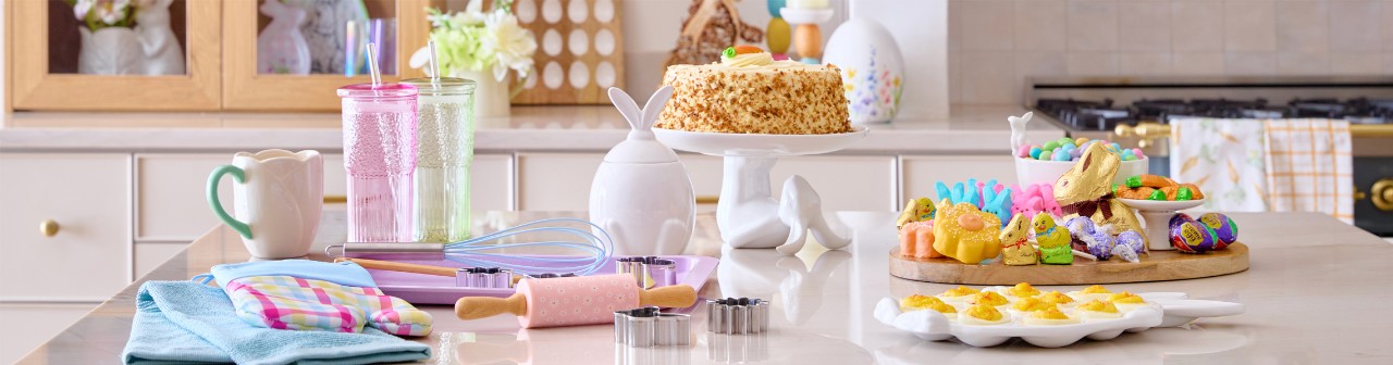 Easter kitchen with wooden egg serving board with candy charcuterie, bunny canister, bunny cake plate, baking items, egg tray, and Easter decor.