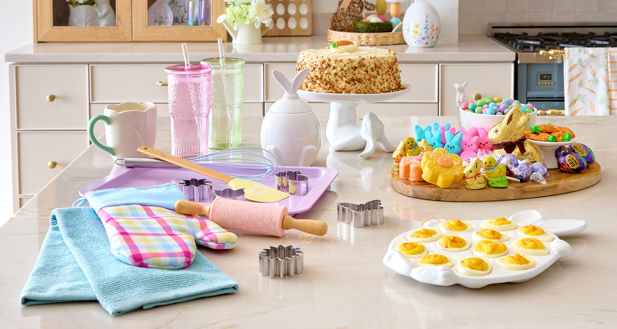 Easter kitchen with wooden egg serving board with candy charcuterie, bunny canister, bunny cake plate, baking items, egg tray, and Easter decor.