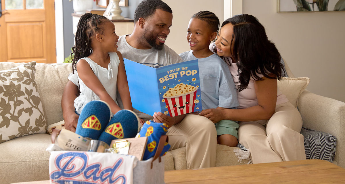 Family on couch with kids, dad reading a Father's Day card with gift basket in foreground
