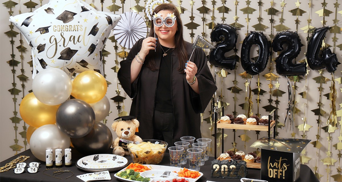 Graduate with photbooth props behind a party table with graduation party supplies, ballons, gifts, and tableware from pOpshelf.