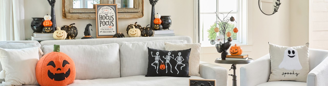 Living room decorated for Halloween with Jack-O-Lanterns in various designs, ghost and skeleton pillows, witch hat and cauldron, skeleton bowl, bat mirror, spider candleholder & more.