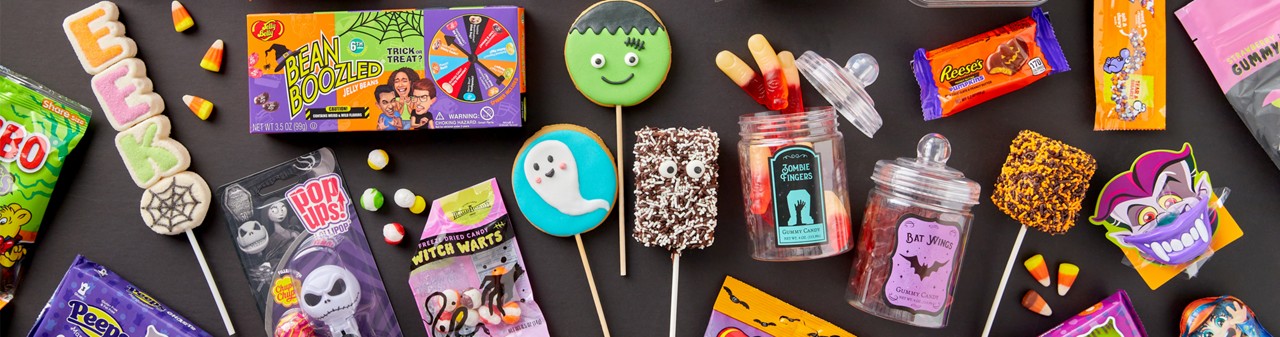 Various colorful halloween candy on a black background: Jelly Belly, marshmallow Peeps and pops, gummy zombie fingers and bat wings, decorated cookie pops, Reese's Pumpkins, Haribo Cears, candy corn, Krispy treats & more.