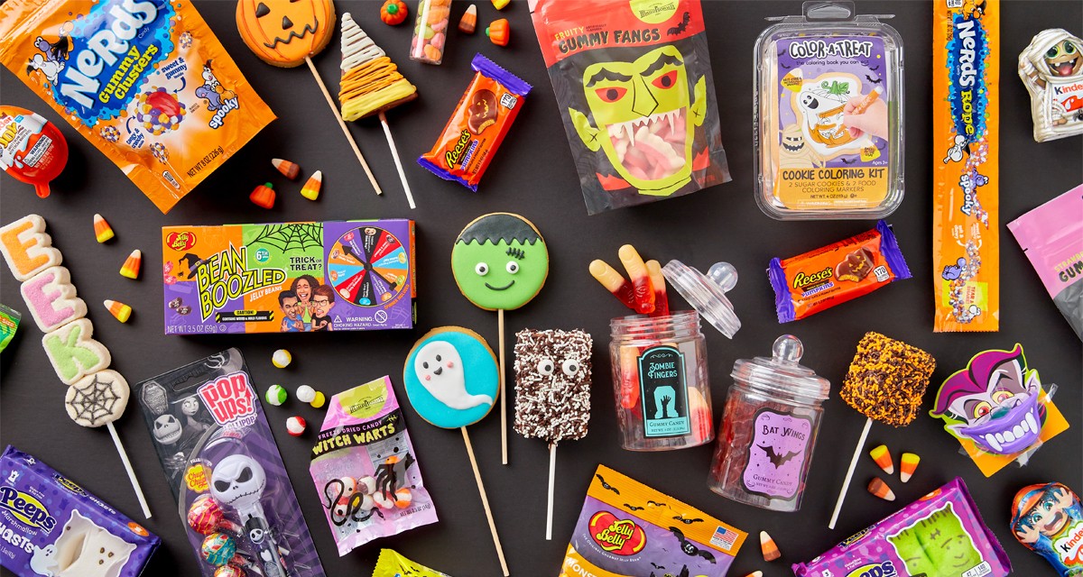 Various colorful halloween candy on a black background: Jelly Belly, marshmallow Peeps and pops, gummy zombie fingers and bat wings, decorated cookie pops, Reese's Pumpkins, Haribo Cears, candy corn, Krispy treats & more.