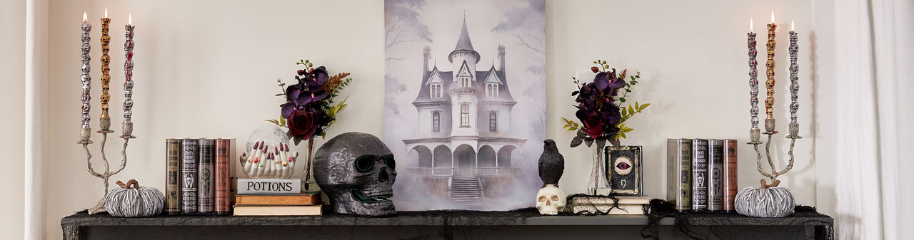 Living room and mantel with spooky Halloween decorations: black metal jack-o-lanterns, ghost and skeleton pillows, skulls, crows, poison bottles, spellbooks & more.