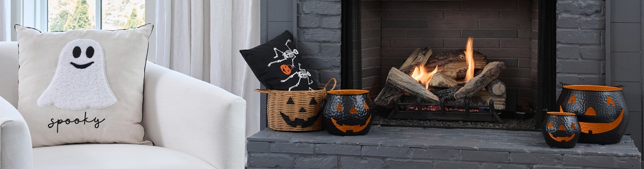 Living room and fireplace with Halloween decorations: black metal, ceramic & wicker basket jack-o-lanterns, ghost and skeleton pillows, skeleton bowl, spider candleholder & more..