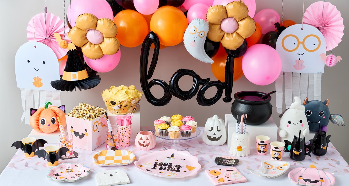 Halloween party table set with party supplies in pastel colors with black accents, a 'boo' balloon & pastel balloon arch, ghost streamers, ghost plates and napkins, and more.