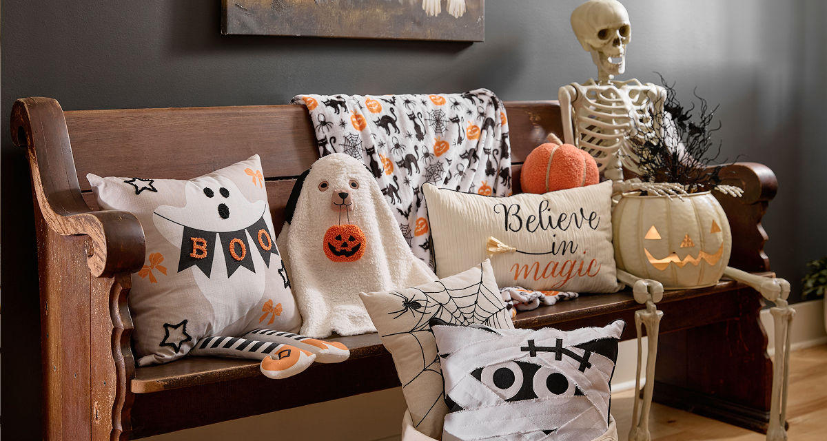 Halloween pillows lined up on a bench in a foyer: dog ghost pillows, mummy pillow, spiderweb pillow, and more.