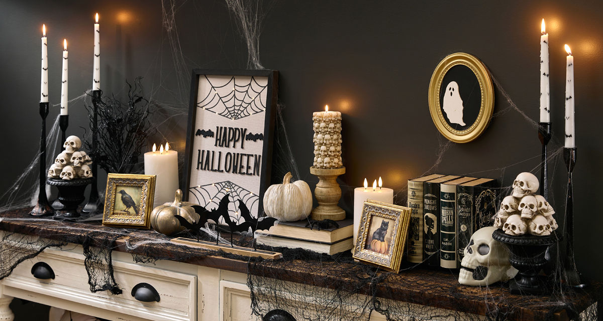 A spooky Halloween-themed foyer table is decorated with classic Halloween decorations from pOpshelf featuring skeletons, Halloween skulls, moody gothic-inspired framed art, bat candlesticks, a spider web tablecloth, golden pumpkins, and more affordable Halloween themed finds.