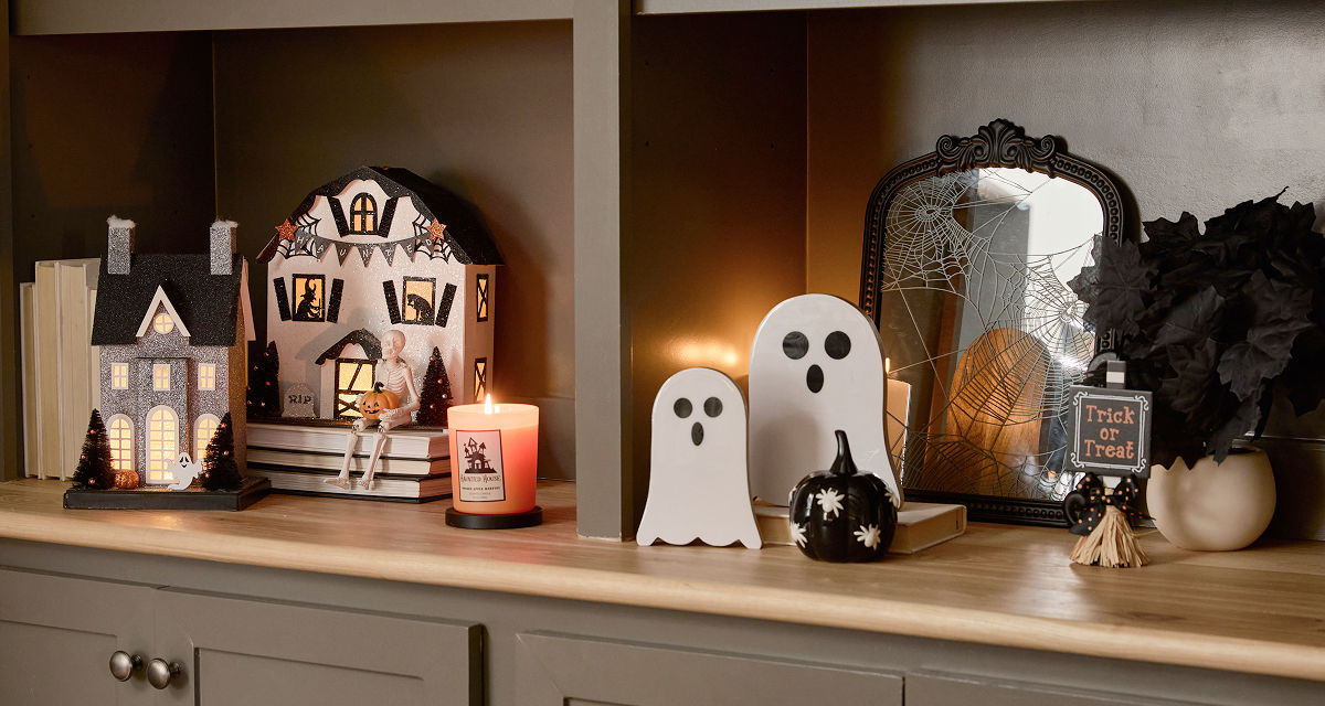 A neutral toned living room  decorated with classic Halloween decor from pOpshelf including ghosts, a spooky cozy blanket, plush pumpkin pillows, viral haunted houses with lights, moody Halloween framed wall art, and seasonal fall candles.