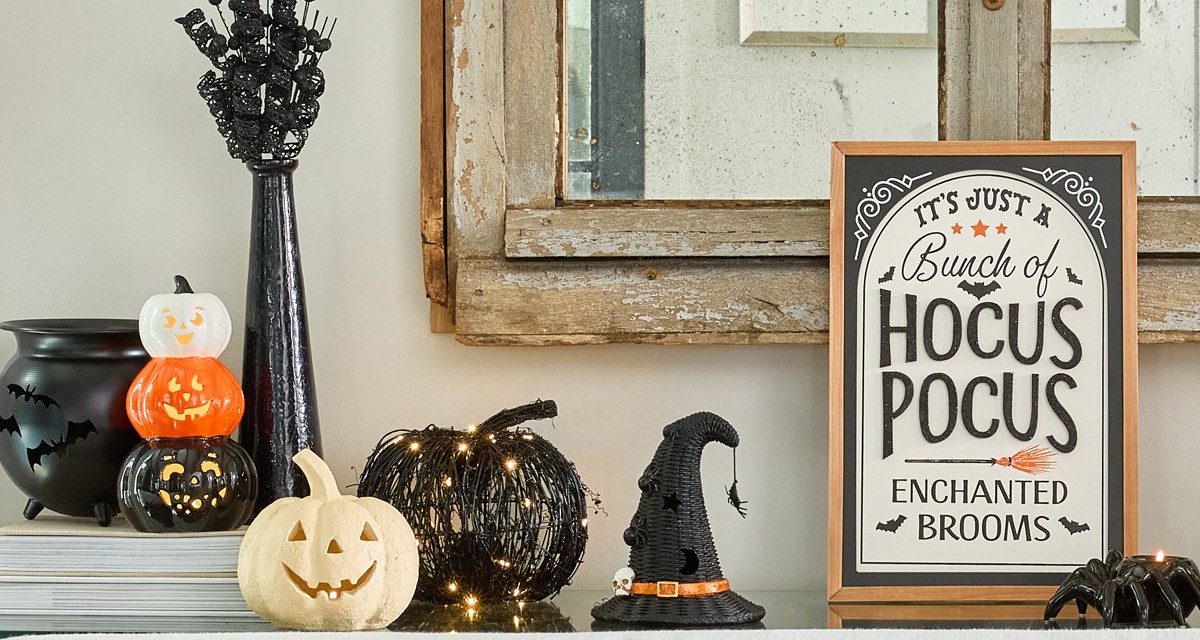 Halloween tabletop decor on console table: black bat cauldron, black wicker pumpkin, stacked pumpkin decor, white jack-o-lanterns & more.